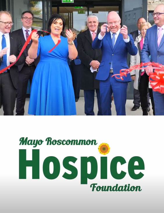 A group of people in formal attire smile and cut a red ribbon at a Mayo Roscommon Hospice event. The Mayo Roscommon Hospice Foundation logo appears below the group.
