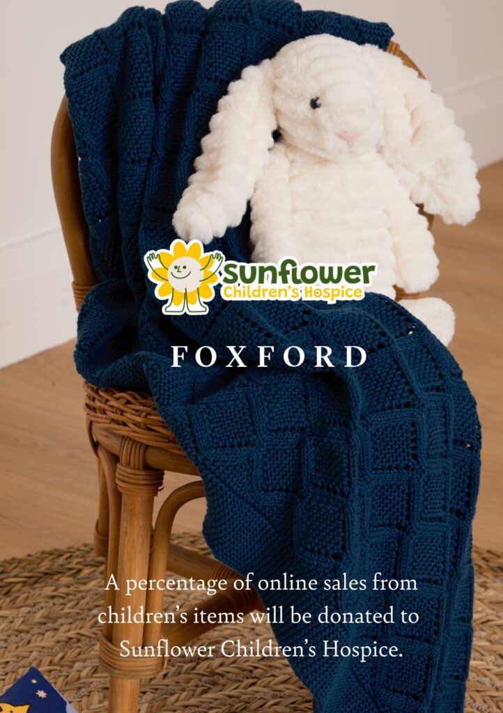 A white plush bunny sits on a wicker chair with a dark blue knitted blanket. Text promotes donations to Sunflower Children’s Hospice and Mayo Roscommon Hospice from Foxford children’s item sales.