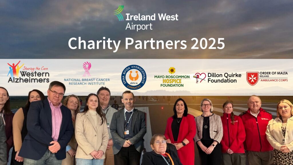 A group of people stands in front of an Ireland West Airport sign, with logos of various charity partners for 2025 displayed above them, including Mayo Roscommon Hospice, Alzheimers, cancer, and ambulance organisations.
