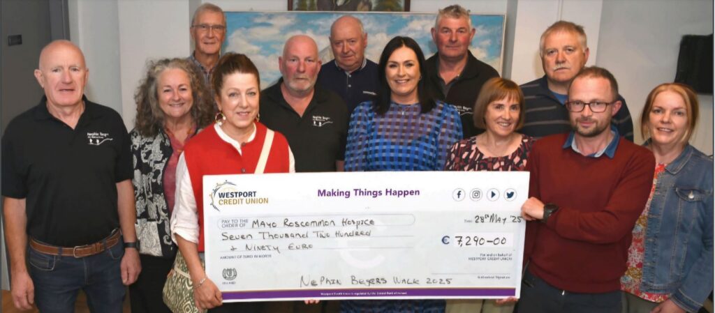 Twelve people standing together, holding a large donation cheque made out to Mayo Roscommon Hospice for €7,290.00 from Nephin Begers Walk 2023. They are smiling indoors in front of a painting, proudly supporting the vital work of Mayo Roscommon Hospice.