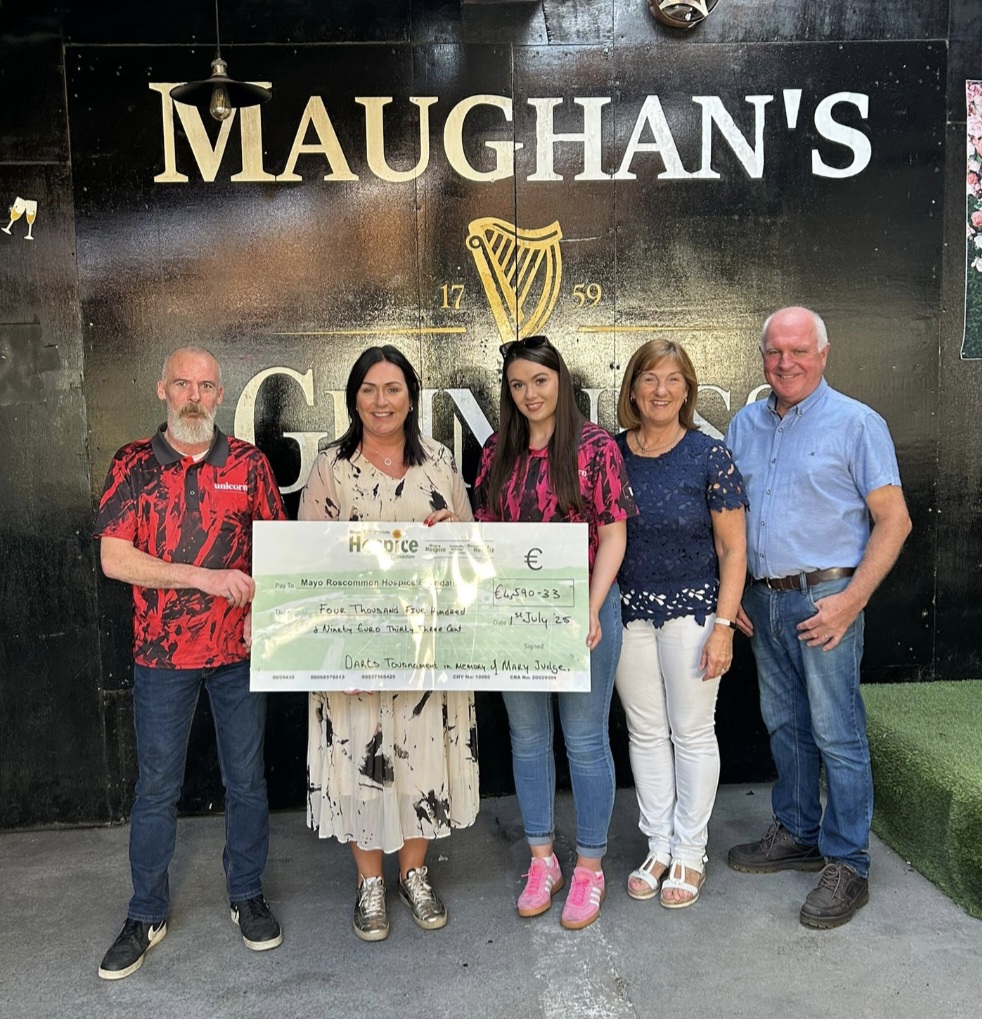 Five people stand together in front of a Maughans Guinness wall, holding a large presentation cheque for €4,240 in support of Mayo Roscommon Hospice. The group smiles for the photo, with the cheque centred between them.