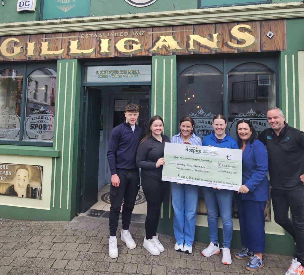 Five people stand outside Gilligans bar, smiling and holding a large charity cheque made out to Mayo Roscommon Hospice, showcasing a generous fundraising donation. The pub’s green façade provides a vibrant backdrop to this celebration in support of the Mayo Roscommon Hospice Foundation.