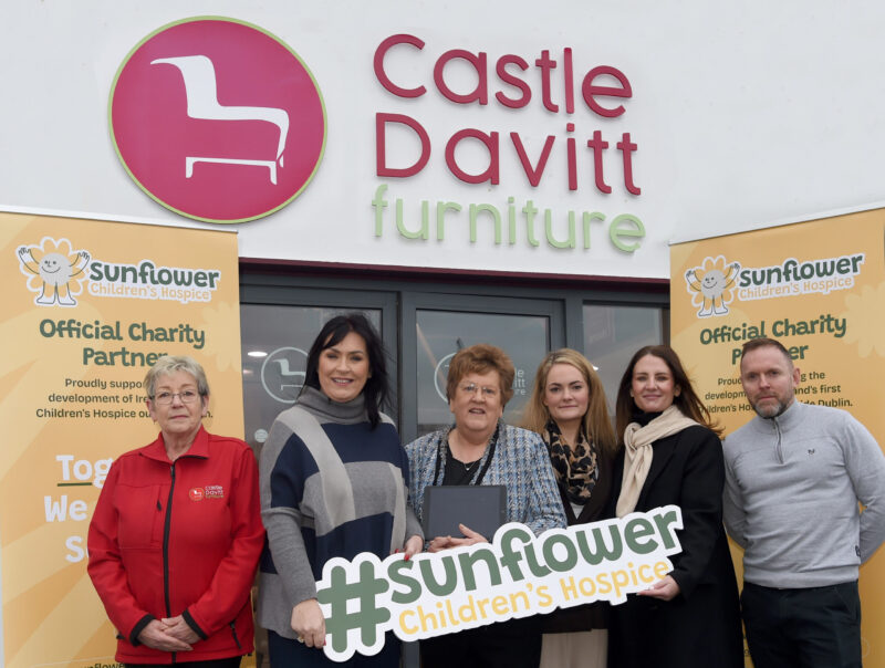 Six people stand in front of Castle Davitt Furniture, holding a #sunflower Children’s Hospice sign, with two Sunflower Children’s Hospice banners on either side, supporting a charity partnership with Mayo Roscommon Hospice.