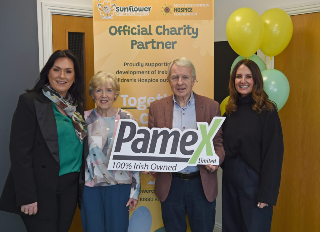 Four people stand smiling together, holding a large Pamex 100% Irish Owned sign. Behind them is a banner for Sunflower Children’s Hospice Foundation, colourful balloons, and a nod to Mayo Roscommon Hospice as the community comes together in support.