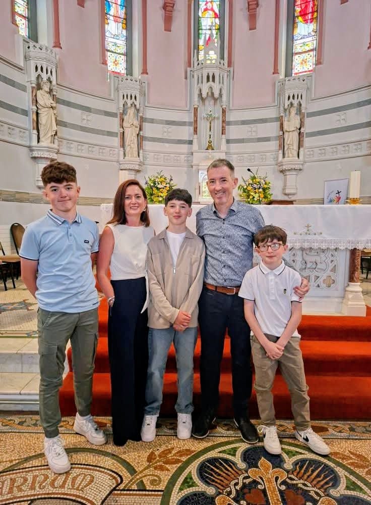 A family of five—two adults and three boys—stand together posing inside a church with stained glass windows, statues, and ornate décor behind them, gathered in support of the Mayo Roscommon Hospice.