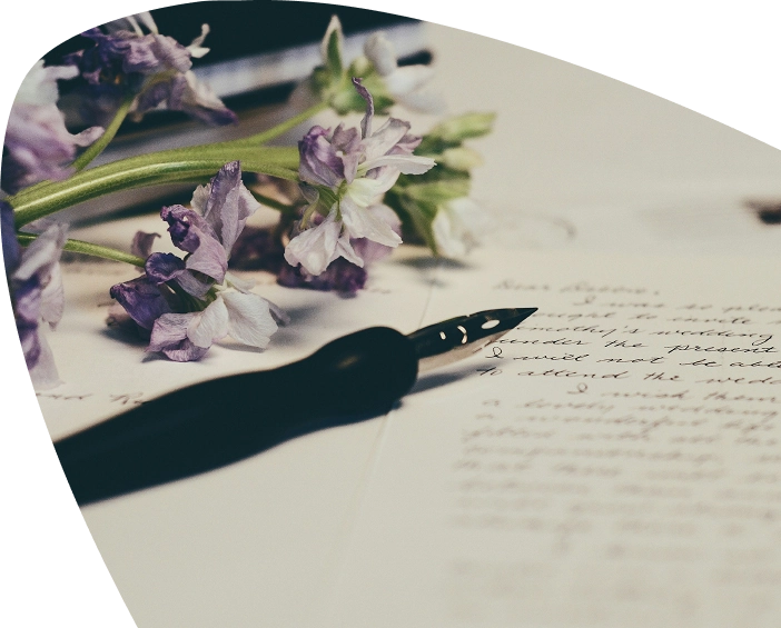 A black fountain pen rests on handwritten paper, with a small bunch of delicate purple flowers in the background, evoking the heartfelt support and compassion offered by Mayo Roscommon Hospice.