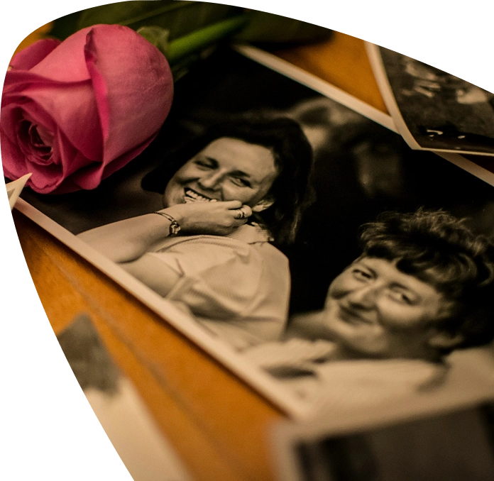 A pink rose rests on black-and-white photos of two smiling women, lying on a wooden surface—a touching tribute reminiscent of the memories cherished by families supported by the Mayo Roscommon Hospice.