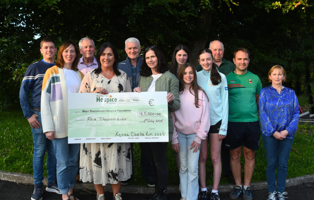 A group of people stand outdoors, smiling and holding a large donation cheque for €5,000 to the Mayo Roscommon Hospice Foundation from the Ronan Clarke Run 2023, proudly supporting the work of Mayo Roscommon Hospice.